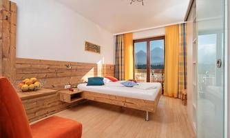 A modern bedroom with wooden walls and large windows. The room is brightly and welcomingly furnished, with a beautiful view of the mountains.