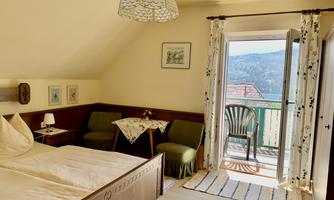 A cozy bedroom with a double bed and a small table. The room has a balcony overlooking the landscape.