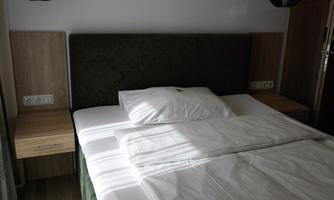 A modern bedroom with a large bed and a nightstand. The room is bright and pleasantly styled.