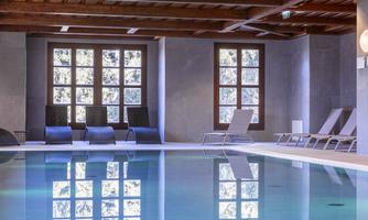 A quiet indoor pool with smooth water and reflective windows. In the background, comfortable loungers are arranged.