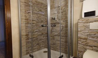 A modern shower with glass walls and an elegant stone pattern. Next to it on the right is a toilet in a stylish bathroom.