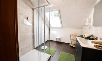 A modern large bathroom with a big shower. There is a window that lets in natural light, as well as a practical washing area.
