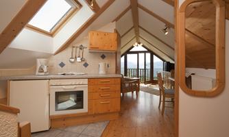 A cozy attic kitchen with wooden details and large windows. The room offers a beautiful view outside.