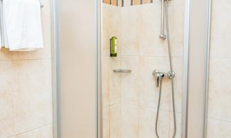 A modern shower cabin with clear glass walls. The walls are decorated with light tiles and it features a handheld shower.