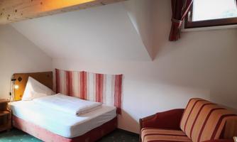 A simple room with a single bed and a cozy seating area. The walls are decorated in bright white with colorful accents.