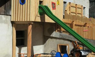 A playhouse with a green slide and colorful windows. In the foreground, several go-karts are on the ground.