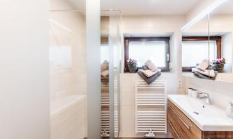 A modern bathroom with a glass shower and a large mirror. The room is bright and welcoming, decorated with wood and white elements.