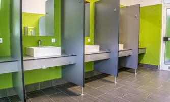 A modern bathroom environment with green walls and gray partitions. The sinks are simply and elegantly designed.