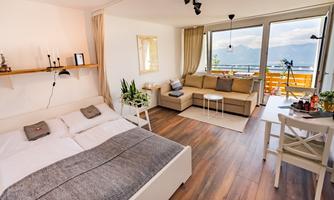 A modern room with a cozy bed and a bright seating area. Large windows provide a beautiful view of nature.