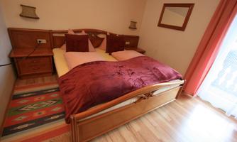 A cozy bedroom with a large bed and red pillows. The room is bright and has a warm wood look.