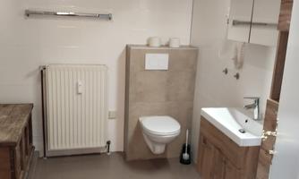 A modern bathroom with a bright design. It includes a toilet, a sink, and a wooden radiator.
