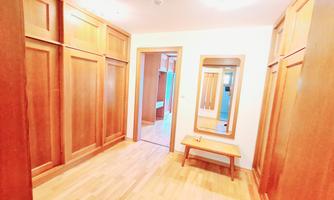 A bright hallway with wooden walls and a large mirror. The floors are made of light wood, and there is a small bench.