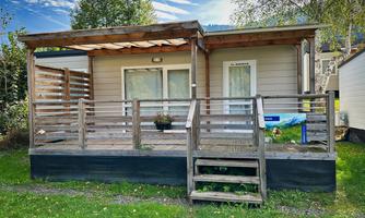 A cozy holiday home with a wooden deck and a small staircase. It is situated in a green environment under a blue sky.