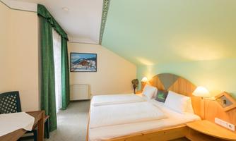 A bright and cozy room with two beds and a small table. The window offers a view of a beautiful景色 and a picture hangs in the background.