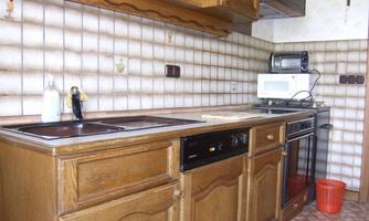 A modern kitchen with wooden furniture, a stove, and a microwave. The walls are decorated with light tiles.