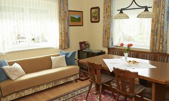 A cozy dining room with a table and chairs. The room has large windows and is equipped with decorative curtains and a carpet.