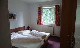 A cozy bedroom with two single beds and colorful curtains. The window offers a view of greenery.