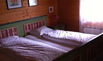 A cozy bedroom with two beds and wooden panels on the wall. There is a window with curtains and a decorative picture on the wall.