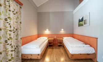 A simple room with two single beds and warm wood tones. The walls are light, and there is a cozy atmosphere.