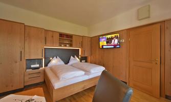 A cozy bedroom with wooden furniture and a television. The room is tidy and well-lit.
