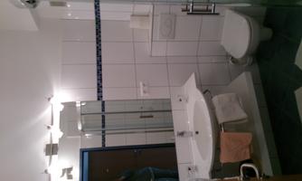 A modern bathroom with a shower, a sink, and a toilet. The walls are brightly tiled, and there are some towels.