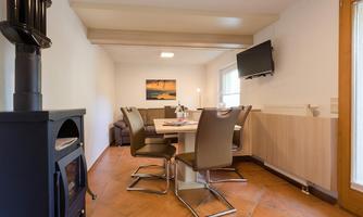 A cozy dining area with a table and chairs. In the background, there is a television and a couch.