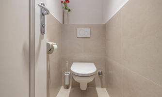 A modern, bright toilet with beige tiles. A small bouquet in a vase adds a friendly touch to the room.