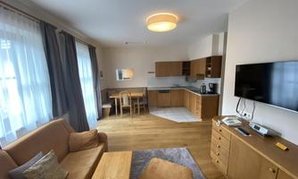 A bright apartment with an open kitchen area and a cozy seating area. The decor is modern and stylish, featuring wood and fabric elements.