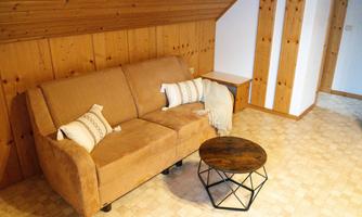 A cozy living room with a brown sofa and a round table. The walls are made of wood and create a warm atmosphere.