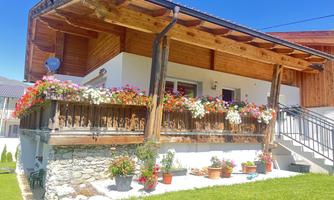 A cozy house with a beautiful balcony adorned with colorful flowers. The lawn is green and well-kept, underneath a bright sky.