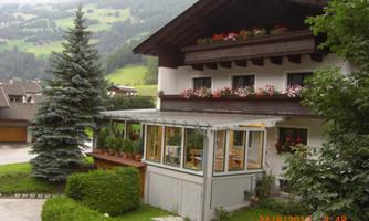 A beautiful house with a balcony and flowers. In the foreground, there is a well-maintained garden and trees.