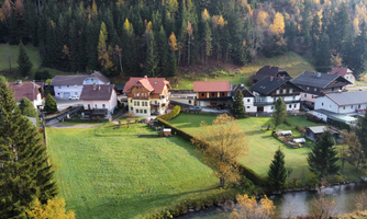 A peaceful landscape with pretty houses and green spaces. Trees surround the scene and a small river flows through the area.