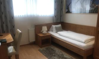 A bright room with a single bed and a small table. On the wall hangs a picture with stylized motifs.