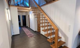 A modern hallway with a wooden staircase. The walls are light and the floor is made of dark tiles.