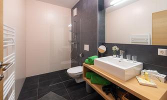 A modern bathroom with a large shower and a stylish sink. There are bright walls, dark tiles, and practical shelving.