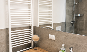 A modern bathroom with a sink and a large mirror. On the wall, there is a radiator and a shower area.