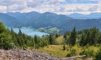 A picturesque mountain landscape with a clear lake and lush forests. In the background, there are tall mountains and a cloudy sky.