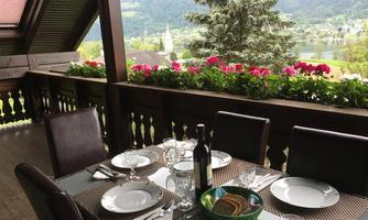 A beautiful dining table on a porch overlooking nature. The table is set with dishes and glasses, surrounded by blooming plants.