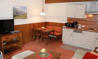 A cozy apartment with an open kitchen and a dining area. The space is bright and modernly designed, with wooden details and a television.