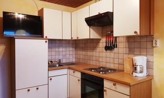 A cozy kitchenette with modern appliances and a television. The walls are in warm colors, and the furnishings are functional.