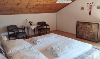 A cozy bedroom with a double bed and two chairs. The wooden ceiling and the decoration give the room a warm atmosphere.