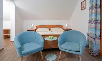 A cozy bedroom with a double bed and two blue armchairs. In the middle, there is a small table with apples.