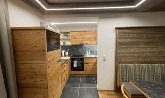 A modern kitchen made of light wood with black work surfaces and new appliances. The space has a cozy atmosphere with a seating bench and modern lighting.