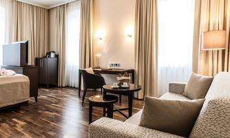 A modern hotel room with a large window and soft colors. There is a bed, a table, and a comfortable armchair.