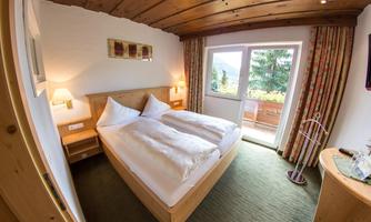A cozy bedroom with a double bed and wooden paneling. There are large windows with a view of nature and a pleasant atmosphere.