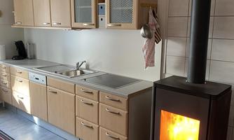 A modern kitchen with a light wood cabinet and an oven. The heating stove radiates cozy light and warmth.