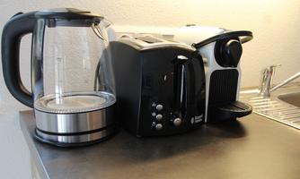 A kettle, a toaster, and a coffee maker are on a countertop. They are designed in modern styles and in neutral colors.