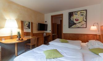 A cozy room with two beds and a modern decor. A colorful painting hangs on the wall, and the room has a warm, inviting atmosphere.