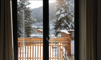 A beautiful view through a window of a snow-covered landscape. In the foreground, there is a balcony with a wooden railing.