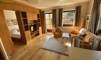 A bright living room with hardwood floor and large windows. There is a cozy seating area and a dining space.